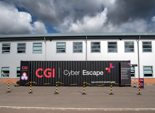 Black shipping container with CGI Cyber Escape branding outside a white building under a cloudy sky.