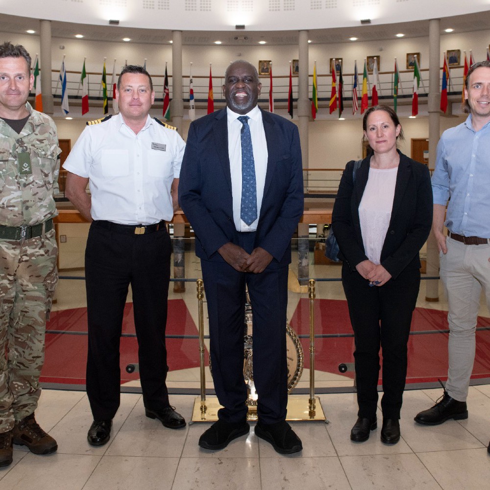 Lord Sewell with military and civilian staff in the Cormorant building forum with international flags in the background.