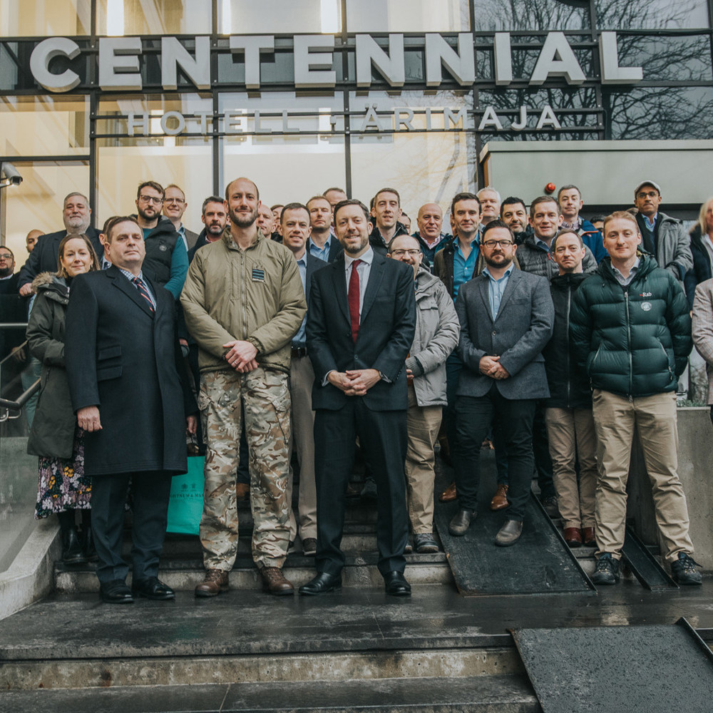 A mixture of people stood in military and civilian clothing outside the Centennial building in Finland. 