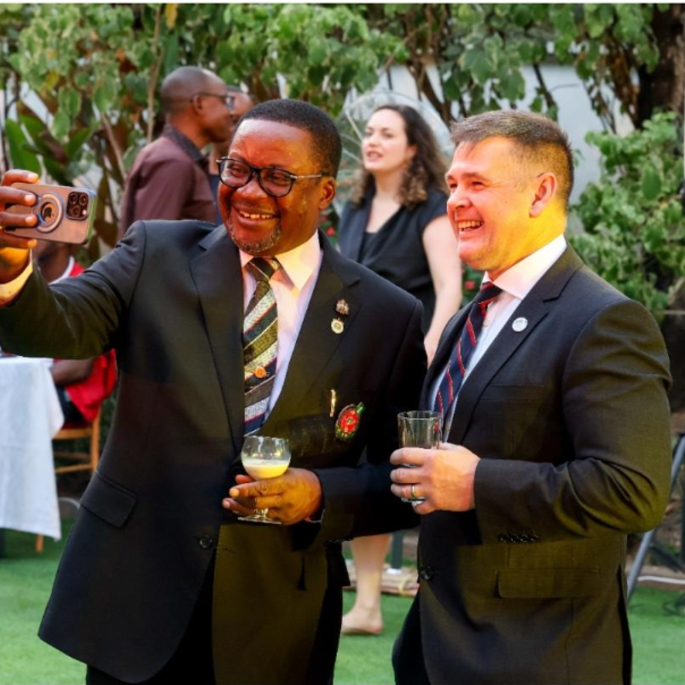 Two men in suits smiling taking a selfie.