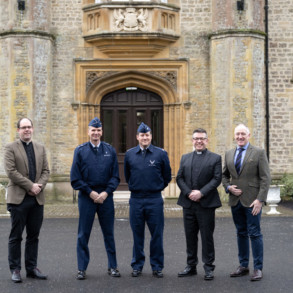 Military Padres and US Air Force officers stood outside an impressive stone grade 2 listed building with a large double wooden door behind them.