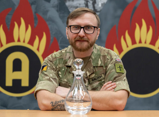 An army officer wearing glasses sat with glass decanter award in front of him. 