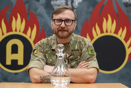 An army officer wearing glasses sat with glass decanter award in front of him. 