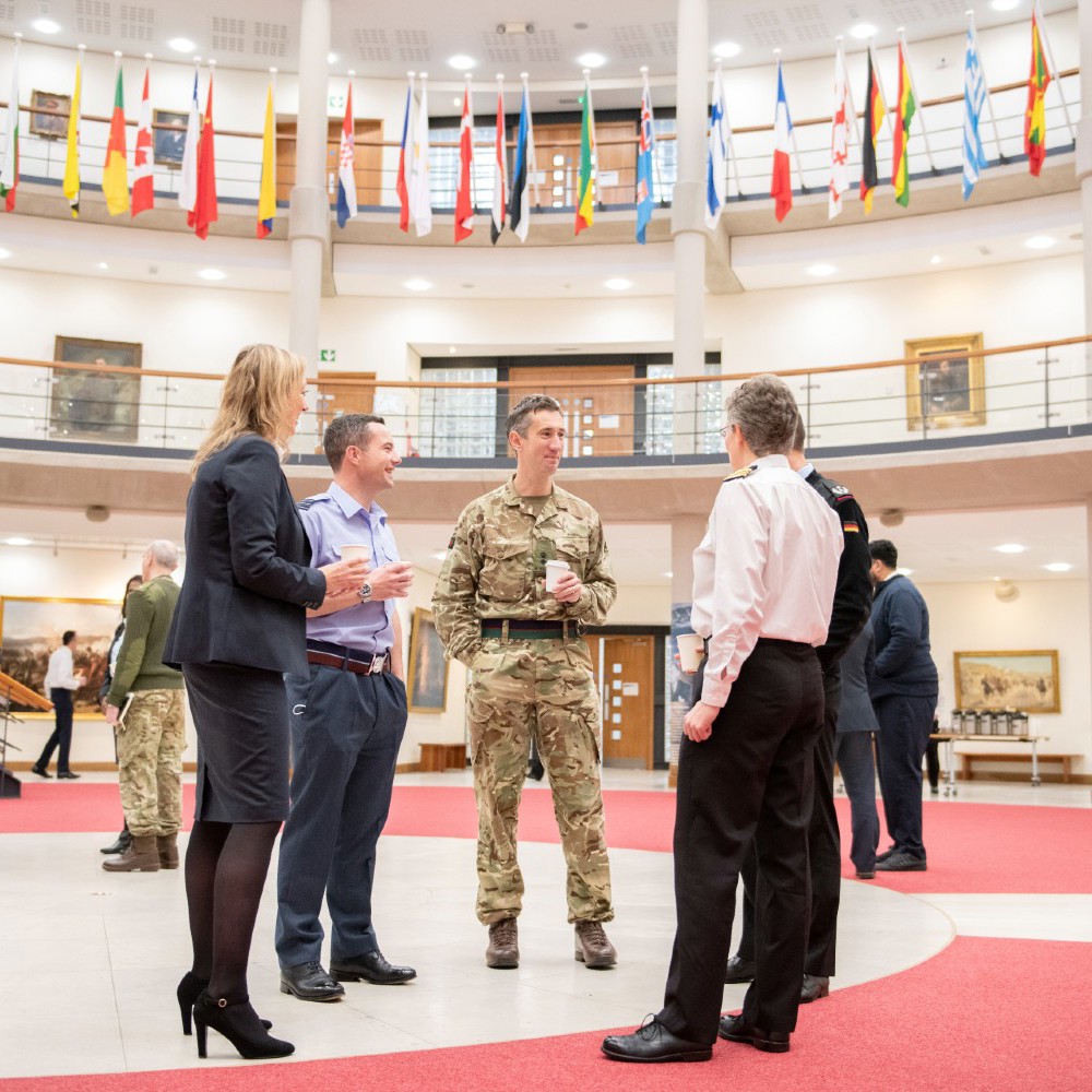 whole force staff gathered in the Forum drinking coffee surrounded by international flags.