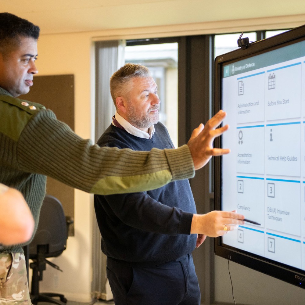 An army officer and civilian pointing to an interactive whiteboard.