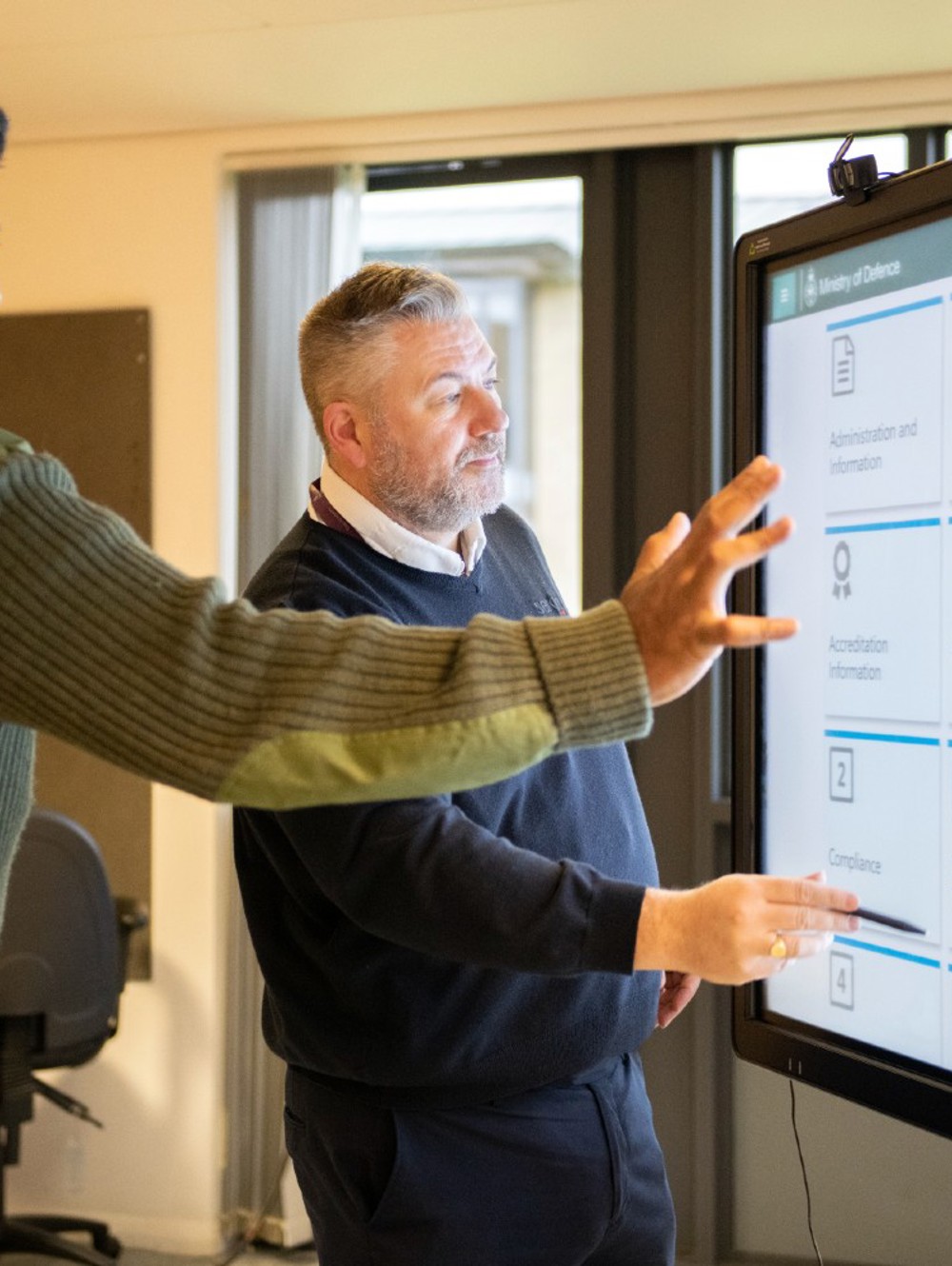An army officer and civilian pointing to an interactive whiteboard.