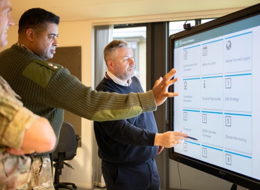 An army officer and civilian pointing to an interactive whiteboard.