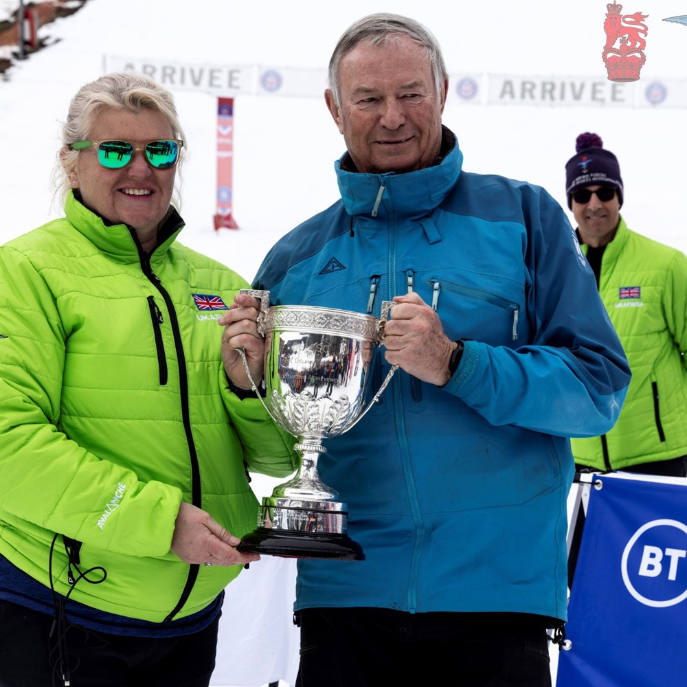 Cdr Nicky Cullen being presented with the Oliver Delaney Trophy in front of snowy ski slopes. 
