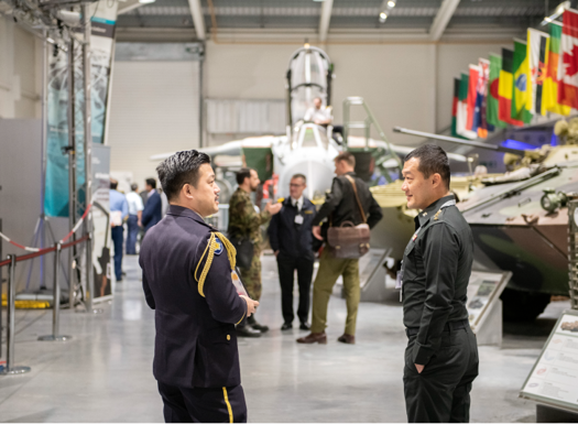Two international students talking inside the DCMCI building with tanks and military kit in the background.