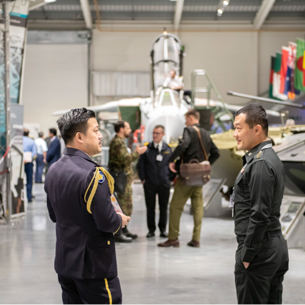Two international students talking inside the DCMCI building with tanks and military kit in the background.