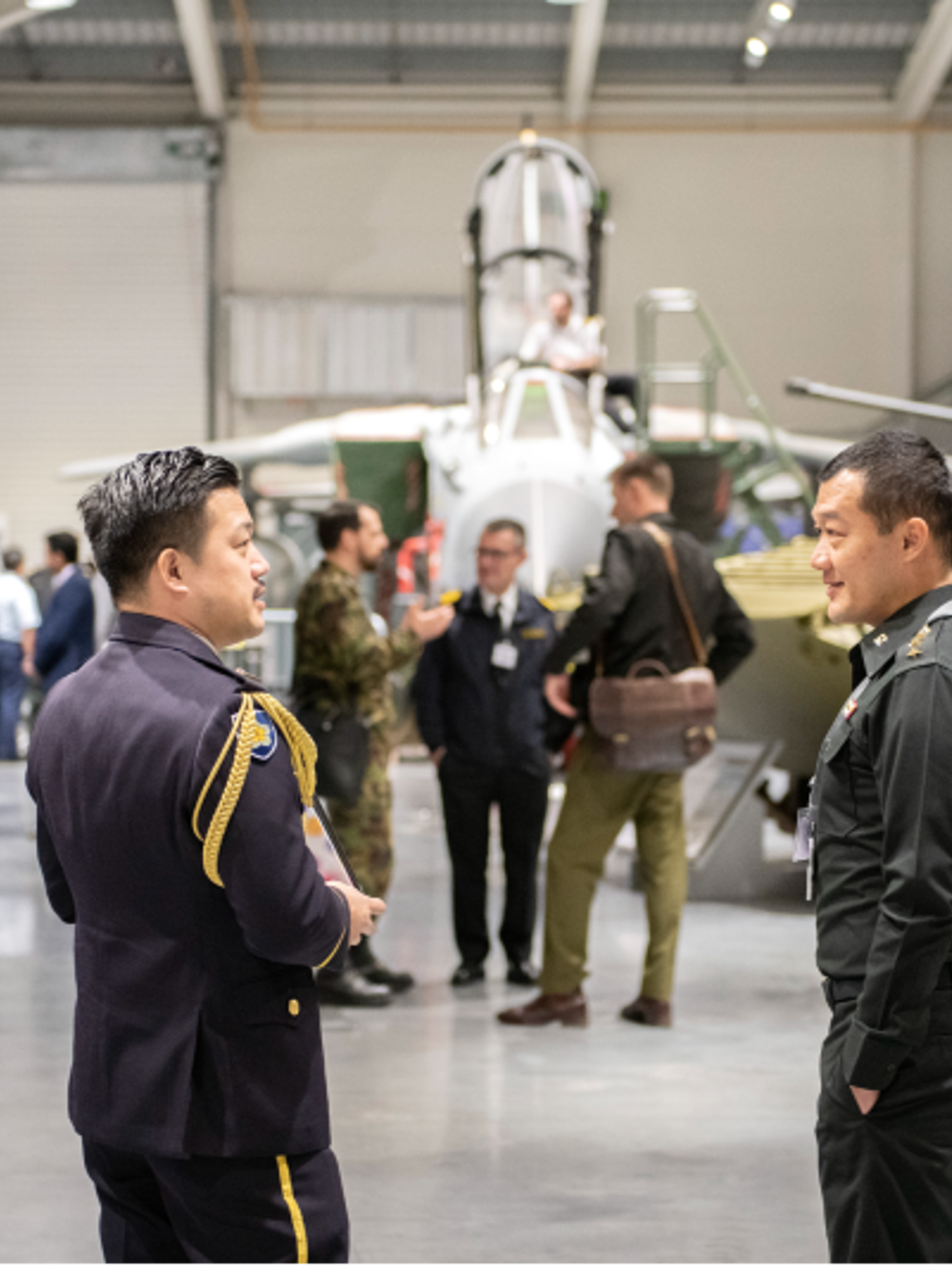 Two international students talking inside the DCMCI building with tanks and military kit in the background.