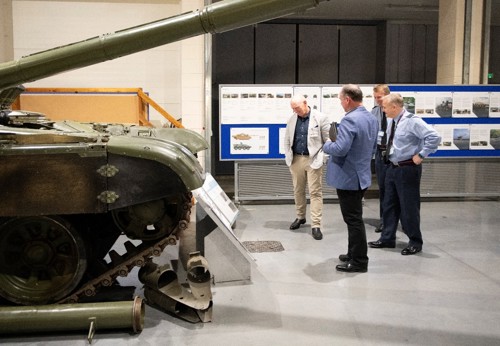 Defence personnel inside a large hall looking at a military tank.