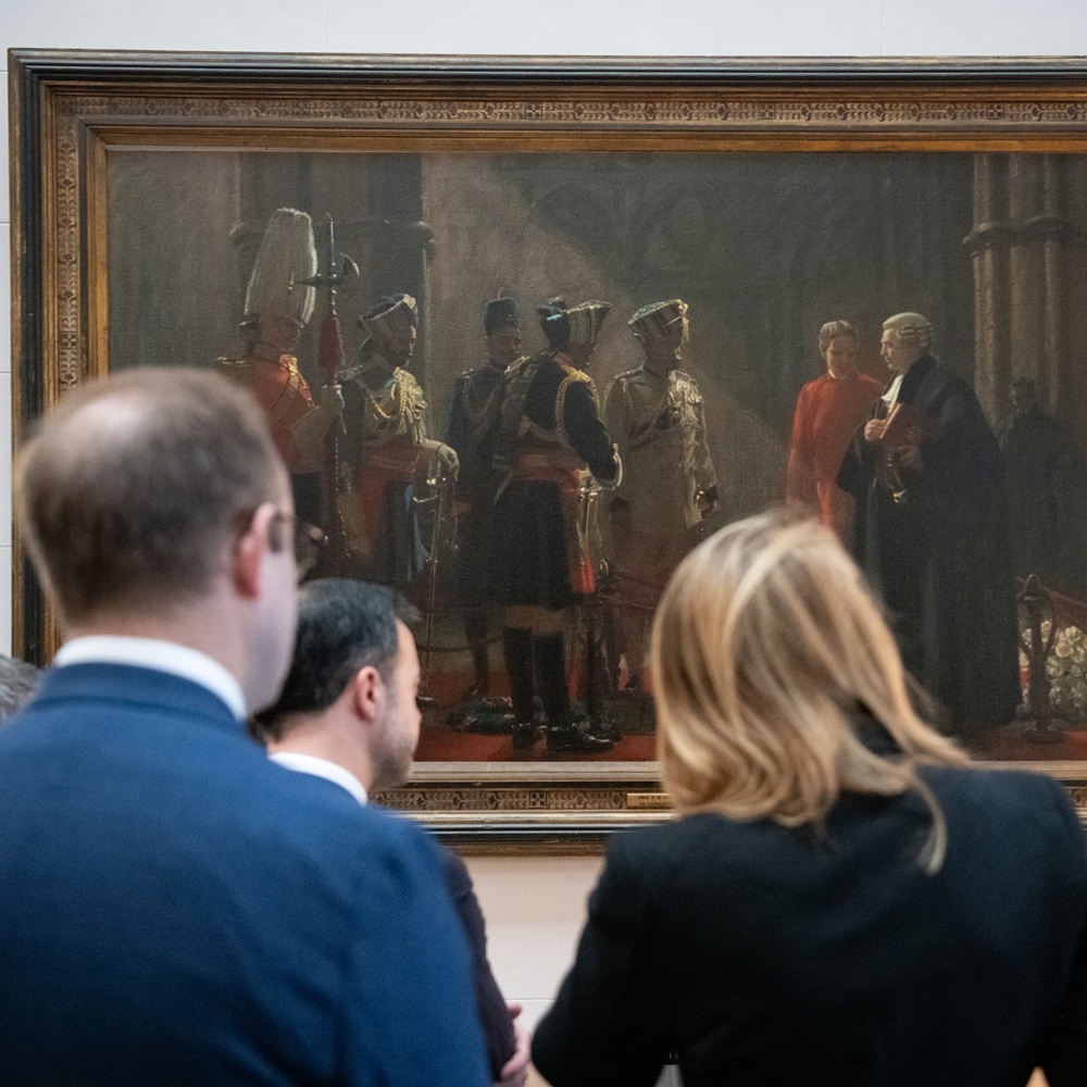 Group of people attentively viewing a large historical painting.