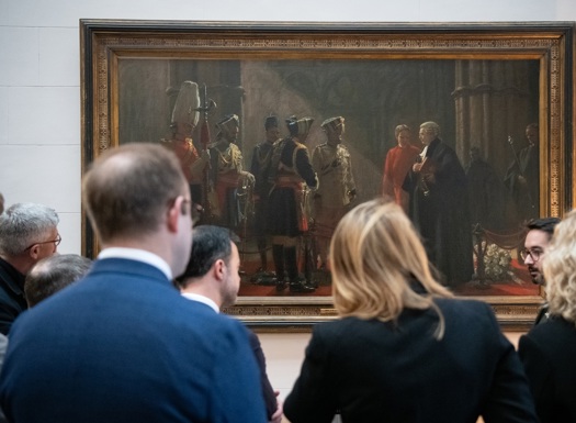 Group of people attentively viewing a large historical painting.