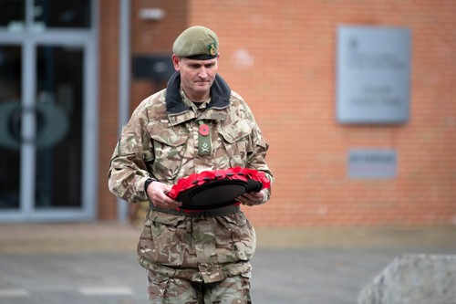 Army officer holding a poppy wreath walking towards a cenotaph.