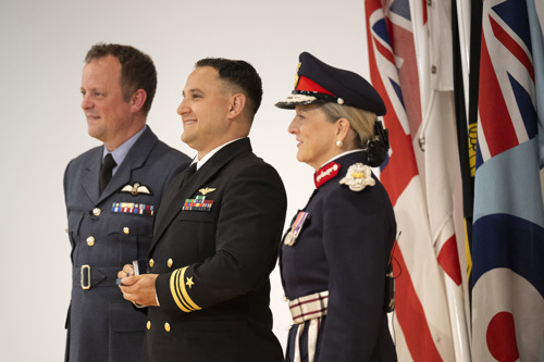 Three people in uniform with military flags in the background.