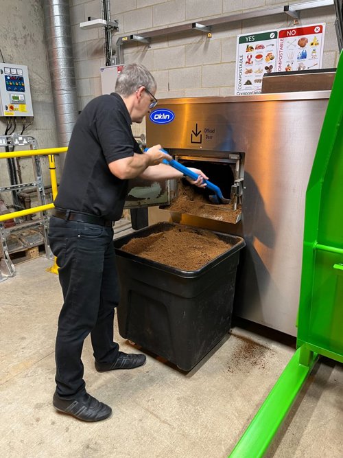 A man emptying compost out of a machine into a black bin.