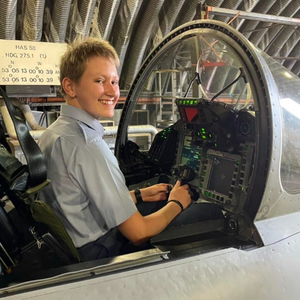 A female officer cadet seated in a cockpit smiling at the camera